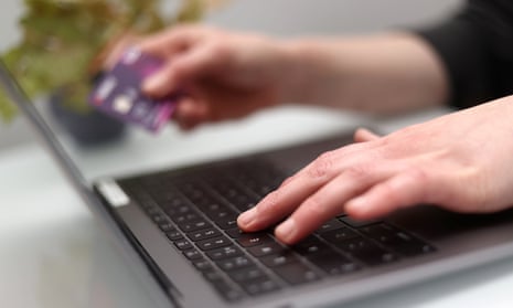 Fingers holding a credit card, above a laptop.