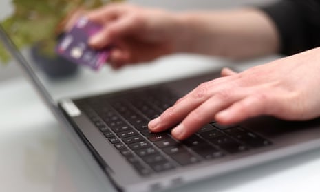 A person holds a credit card in one hand, while typing on a laptop with the other.