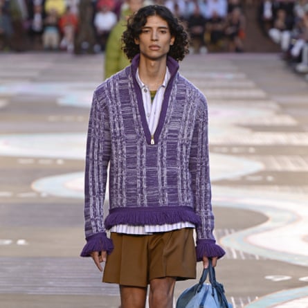 Model on the runway at Louis Vuitton show wearing purple quater-zip jumper with flared sleeves and a white undershit.