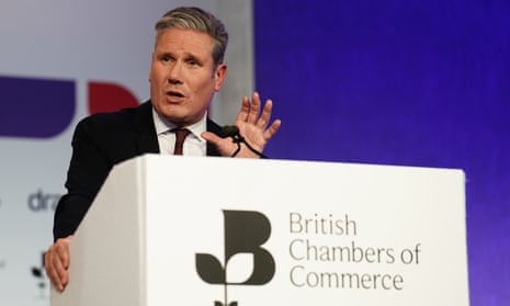 Keir Starmer, in a shirt, tie and blazer, speaks with his hand in the air at a podium that says "British Chambers of Commerce"