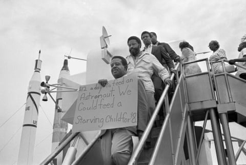 The Rev Ralph Abernathy, flanked by associate Hosea Williams stand on steps of a mockup of the lunar module displaying a protest sign while demonstrating at the Apollo 11 moon launch.