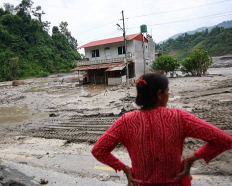 A woman looks on as heavy machinery works in the aftermath of deadly flash floods and a mudslide near the Nepal-Tibet border