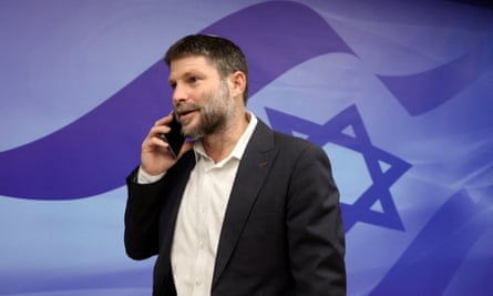 Bezalel Smotrich talking on a mobile phone against a backdrop of an Israeli flag mural