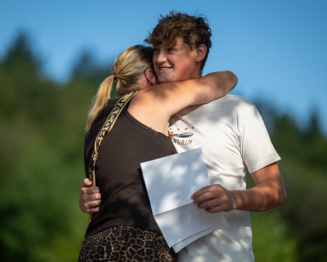 Woman hugs boy against backdrop of out of focus trees and blue sky