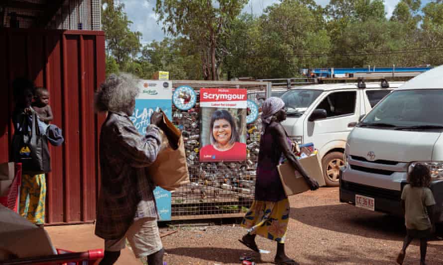 People walking out with groceries at Ramingining supermarket in the Northern Territory, past signs for Labor’s Lingiari candidate Marion Scrymgour.