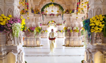 Modi, lit from behind, walking through a beautiful temple with wide pillars adorned with flowers