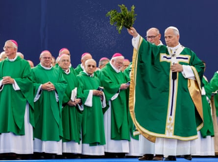 Pope Leo sprinkles holy water with a leafy branch before bishops during an outdoor Mass in Lourdes, France.