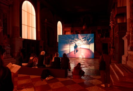 Visitors sit in a darkened room watching a video of a man performing acrobatics on a pole