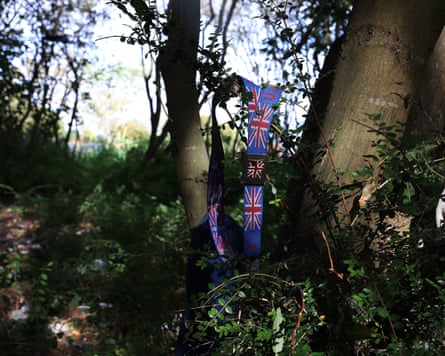 A Union Jack belt hangs from branches in woodland near a Calais migrant camp