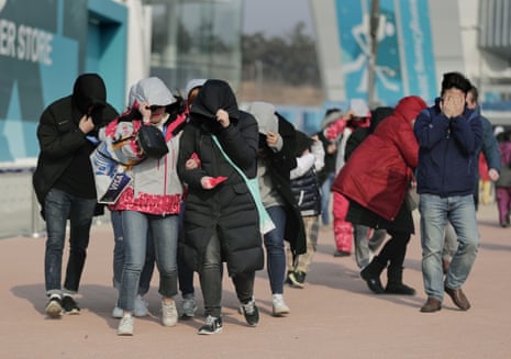 Visitors to Gangneung Olympic Park shield themselves from strong winds as they leave the area.