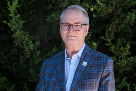 Adam Hamilton, Kansas Senate candidate, stands outdoors in a plaid blazer before greenery