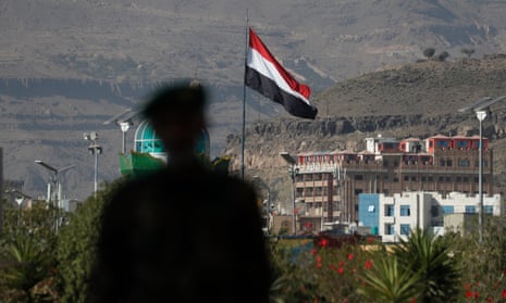 The silhouette of a person walking past a Yemeni flag fluttering in Sana'a