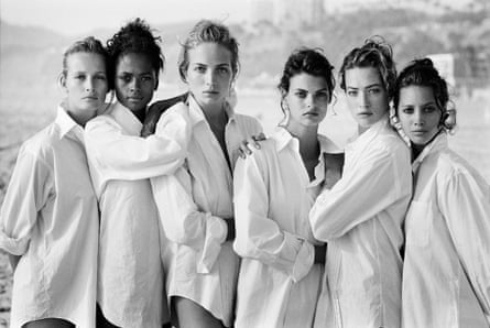 Supermodels in white shirts stand sandwiched against each other on a beach