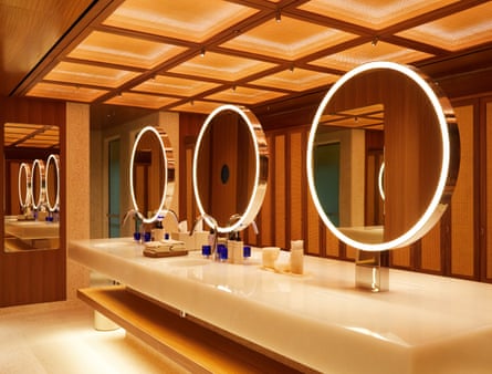 Three large lit-up round mirrors on a long beige marble and teak table, reflected by a long mirror at the end, with square lighting above