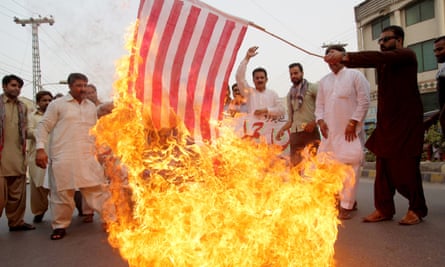 A Pakistani demonstrator holds a burning US flag as others protest against a drone strike in Balochistan.