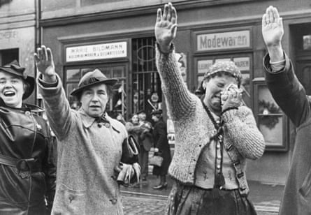 Black and white image of women raising their right hands in a Nazi salute. One of the women holds a handkerchief to her face as she weeps