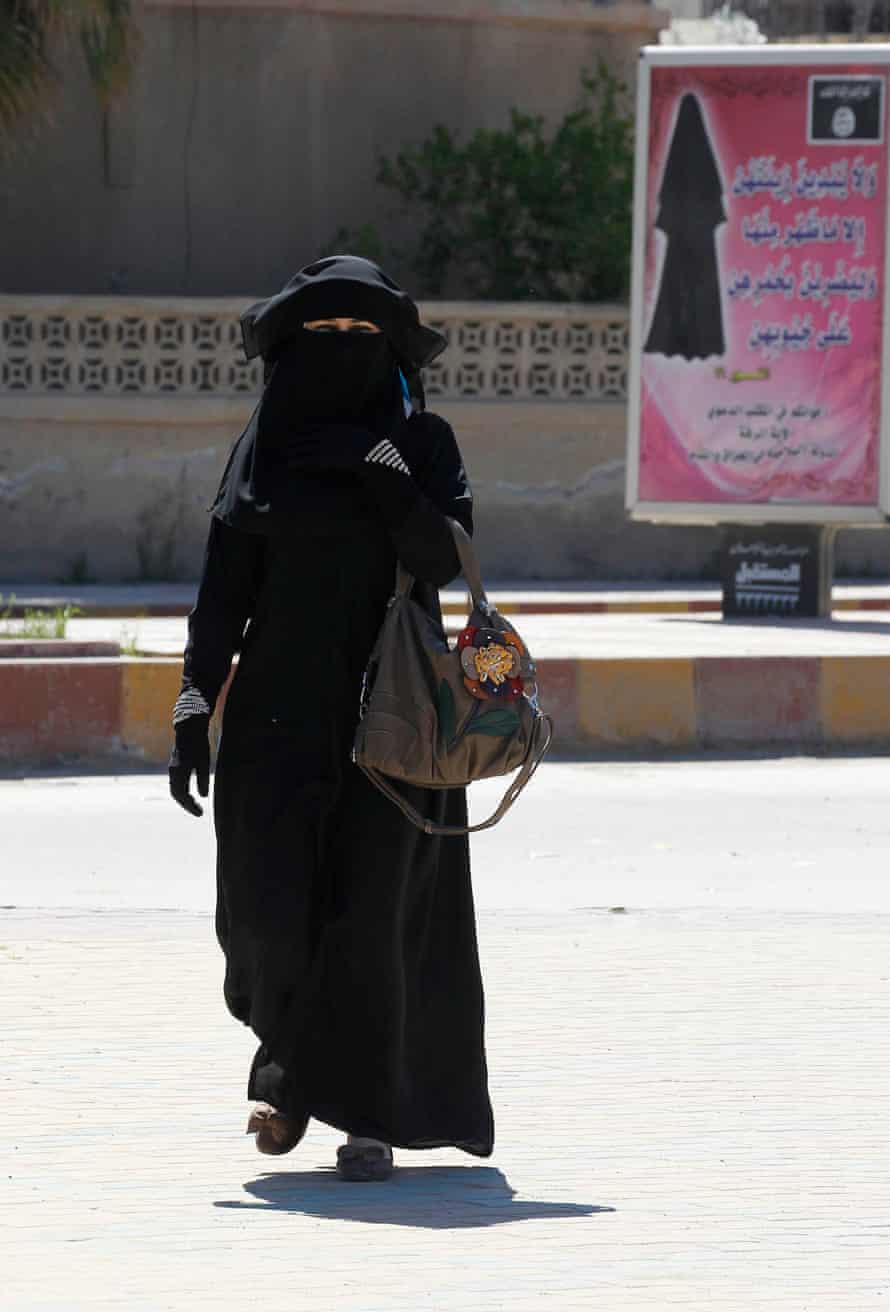 In Raqqa, a woman walks past a billboard that carries a verse from Qur’an urging women to wear a hijab