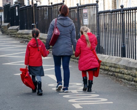 A mother walks with her two children near a school