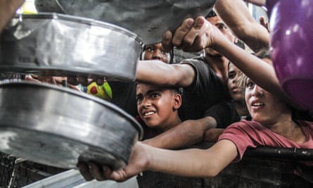 Displaced Palestinians hold pans to receive food.