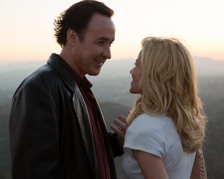 Cusack, in leather jacket, stands close to Elizabeth Banks in front of a sunset