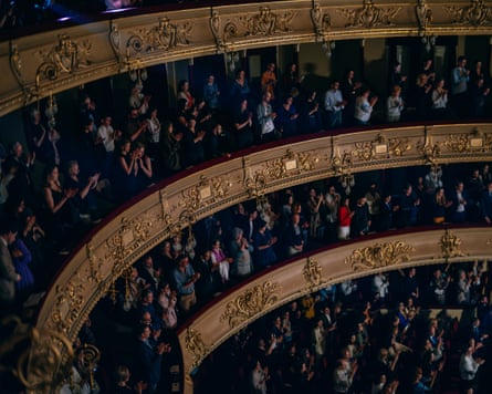 Audience members in tiered seats give a standing ovation