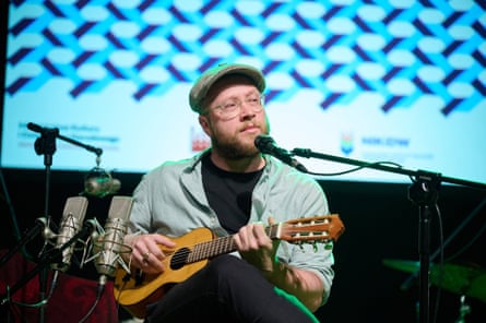 A man sits on stage playing a gitalele.