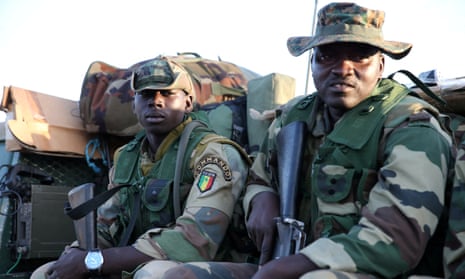 Two Ecowas soldiers carrying guns sit on a military vehicle