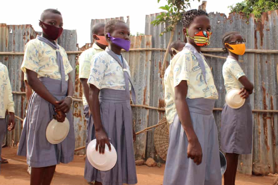 Female students wearing face masks wait in line with their dishes at lunchtime during the Covid-19 pandemic in Tori of Ouidah, Benin, March 2021.