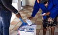 A woman leans down to place her voting paper in a ballot box