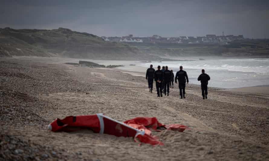 Police patrolling the beach in northern France pass by the wreckage of a inflatable boat