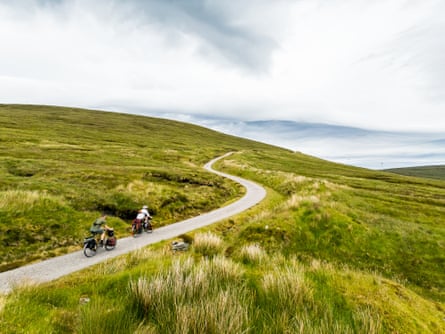 Two men cycle a winding road over the brow of a hill