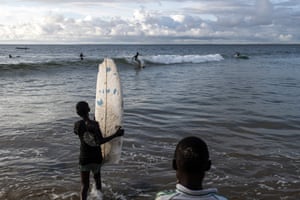 A young surfer enters the water with a broken surfboard in Robertsport