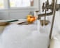 A bubble bath with the tap running and a book and a candle on the side