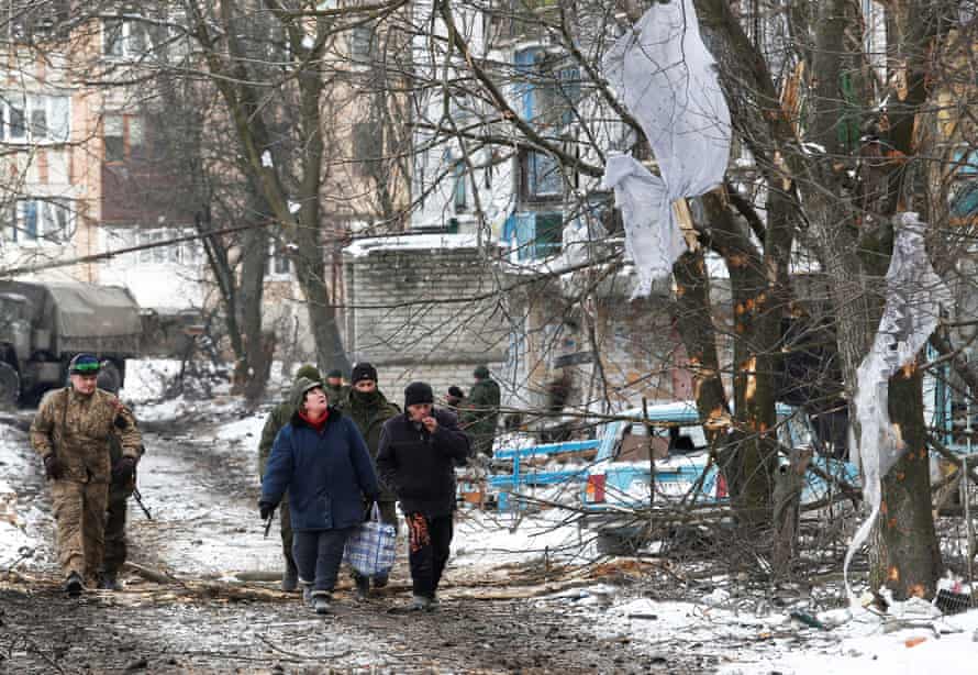 Local residents and service members of pro-Russian troops in uniforms walk past a residential building which was damaged during the conflict.