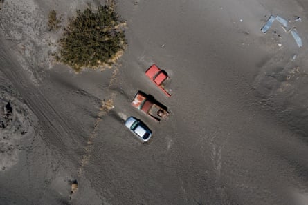An aerial shot of two red trucks and a silver car buried in dust.