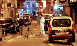 A forensic officer and a police officer stand next to a numbered reference index pad and a camera on a tripod near the scene of the crime in Paris.