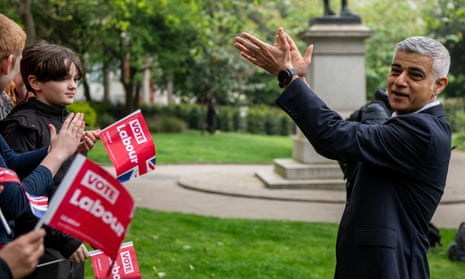 Sadiq Khan clapping his hands in front of a group of young people waving Labour flags in a park