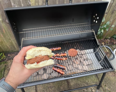 Argos barbecue with meat on while a hand shows a hamburger in the foreground