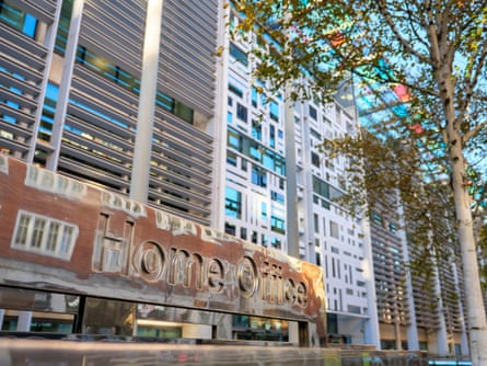 The modern Home Office building in Westminster. It has a metal sign at the front which is reflecting the images of brick buildings on the other side of the street.