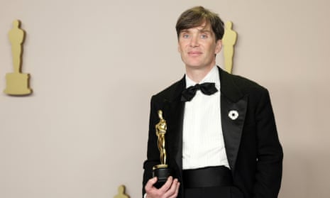 A man in a tuxedo stands holding a golden Oscar statuette