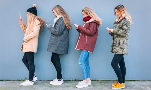 Four young women standing in a row using their cell phones
