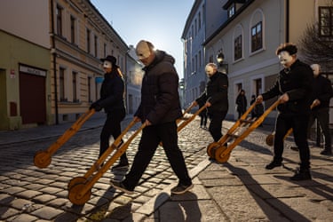 Image 14: People wearing masks push wooden rattles across a cobbled street