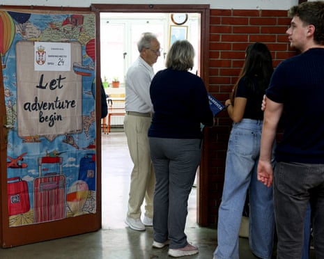 Voters queue at a Serbian polling station doorway decorated with a travel-themed poster