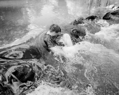 A man rests in the river with water pouring over him