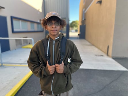 A boy wearing a green jacket, glasses and a backpack posing for the camera