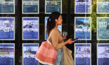 A woman walks past a real estate store offering homes for sale and for rent