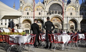 Waiters stand by empty tables in a cafe in St Mark's Square in Venice