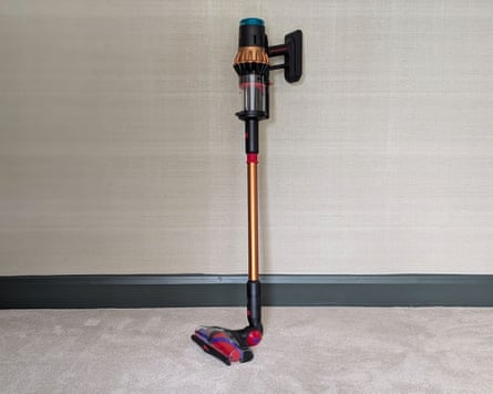 A Dyson V16 vacuum propped up against a wall in a carpeted room