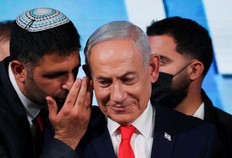An aide whispers to Israeli PM Benjamin Netanyahu, who smiles in a suit and red tie