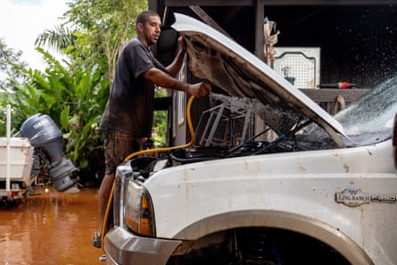 A man sprays water from a hose at mud in a car engine